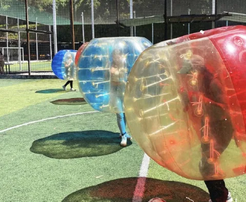 Esferas de bubble ball en juego sobre una cancha sintética de fútbol con malla perimetral